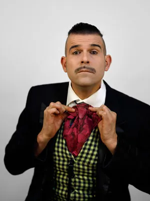 Butler Herrmann hält in beiden Händen silberne Dollar, trägt einen schwarzen Frack und eine gelbe Weste, sein Blick ist streng und seine Haare sind nach hinten gegelt