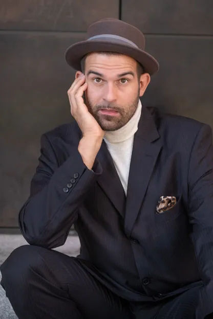 Elias Elastisch in einem dunkelblauen Nadelstreifen-Anzug, trägt einen Hut und einen weißen Rollkragen-Pullover, hat einen Drei-Tage-Bart, aufgenommen auf der Museumsinsel in Berlin