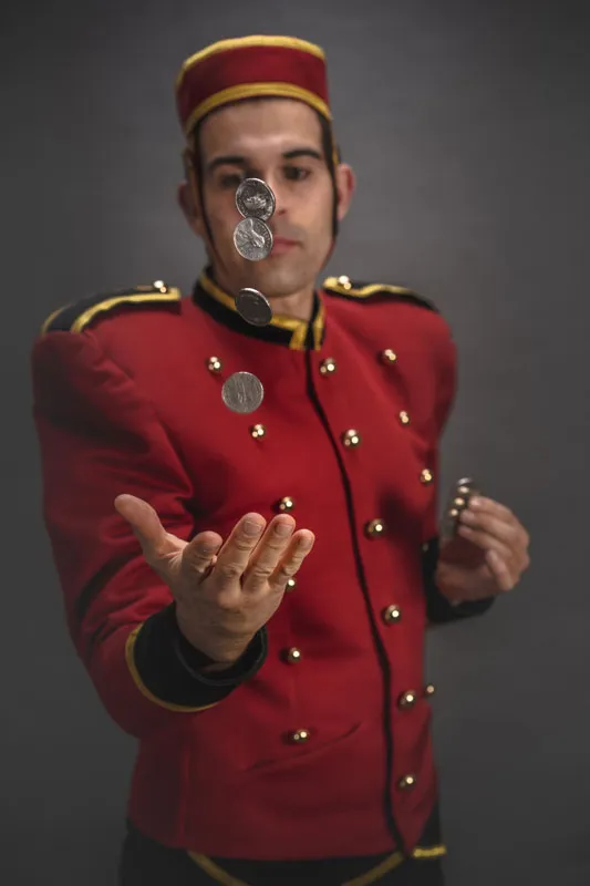 Page Jacques Liqueur trägt eine edle rote Uniform mit goldenen Knöpfen, wirft 4 Silbermünzen aus seiner Hand in die Luft