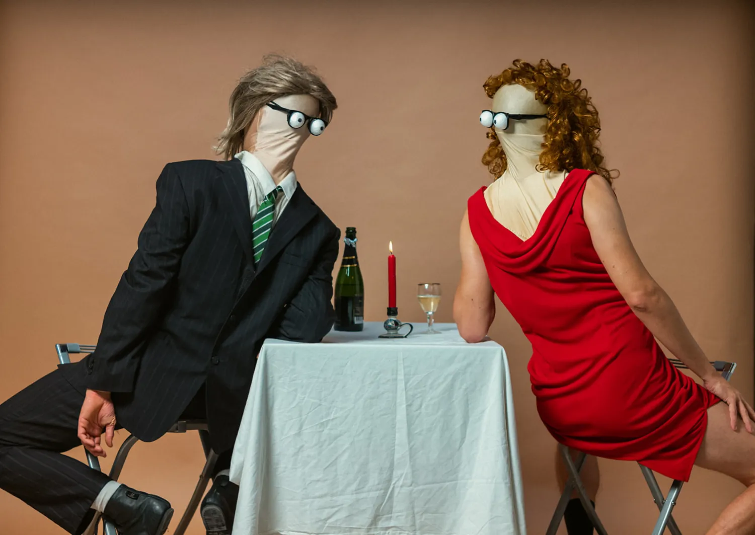 Zwei maskierte Figuren von Duo Mimikry im Anzug und roten Kleid an einem Tisch mit Kerze