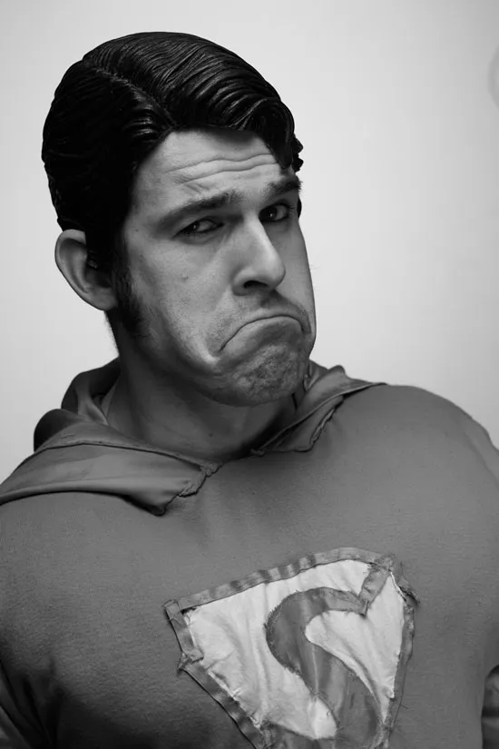 Superman in Schwarz-Weiß-Foto, trägt eine Gummiperrücke und guckt wie ein Affe in die Kamera