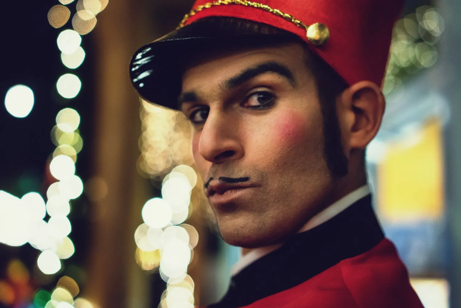 Nussknacker von Elias Elastisch: Mann in roter Uniform und rotem Hut vor funkelnden Weihnachtsmarkt-Lichtern